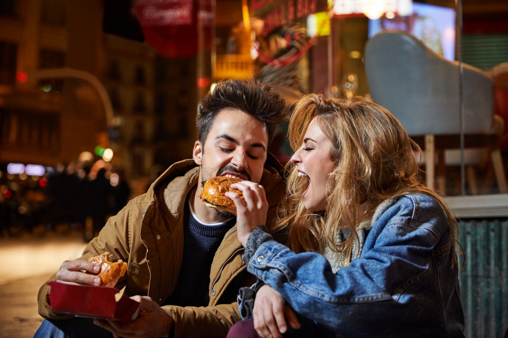Male and female couple eating burgers, female feeding male.